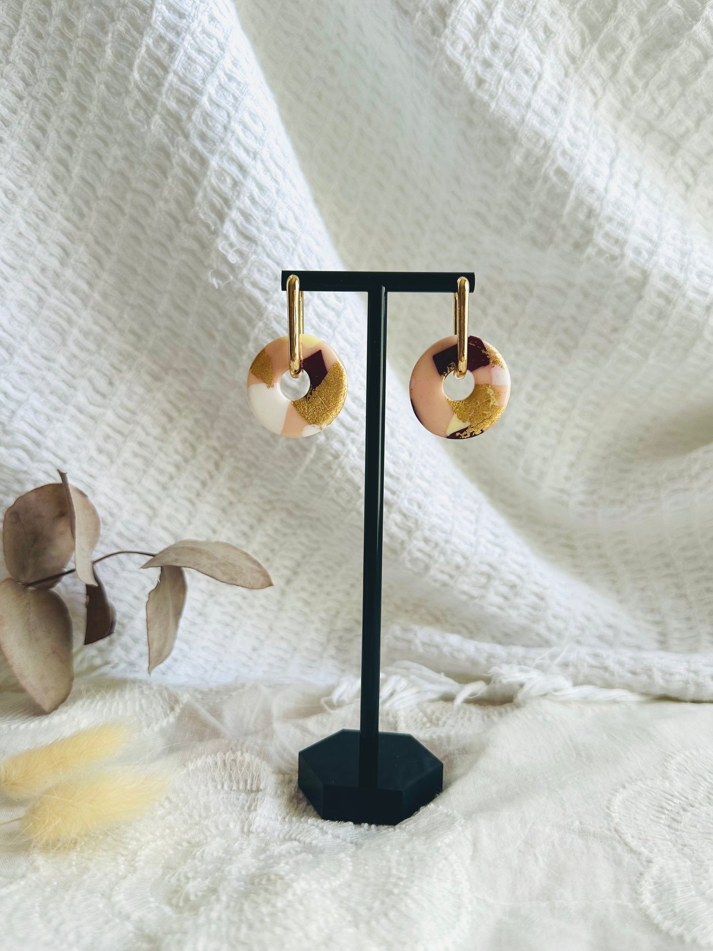 Pendiente donut grande, aro alargado, tono blanco, beige, granate y dorado.