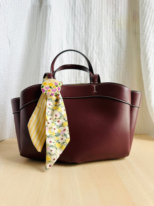 Adorno para bolso amarillo con flores lilas y blancas.