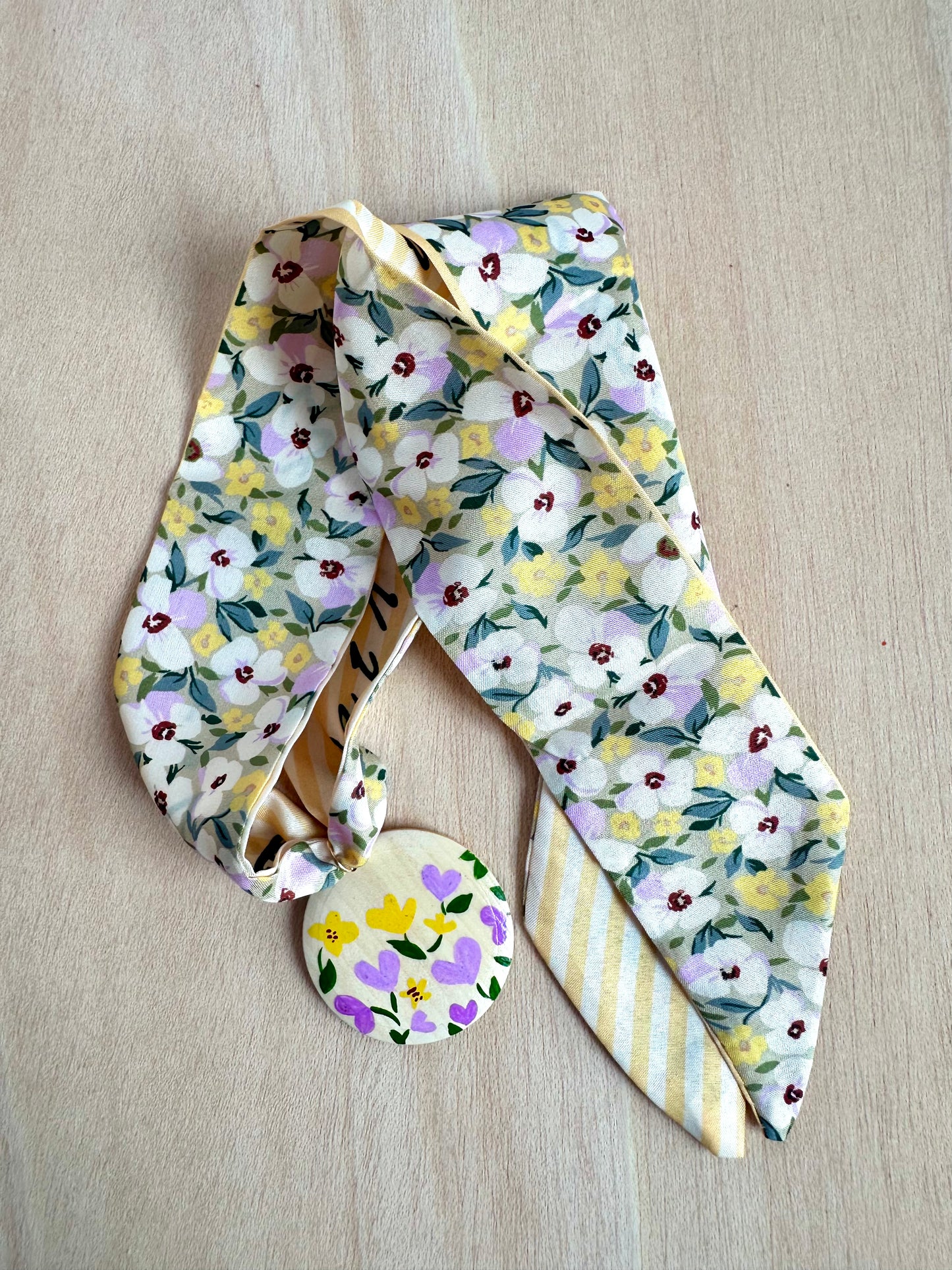 Adorno para bolso amarillo con flores lilas y blancas.