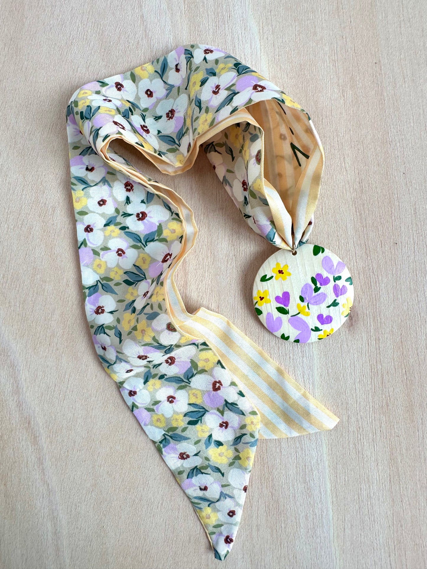 Adorno para bolso amarillo con flores lilas y blancas.